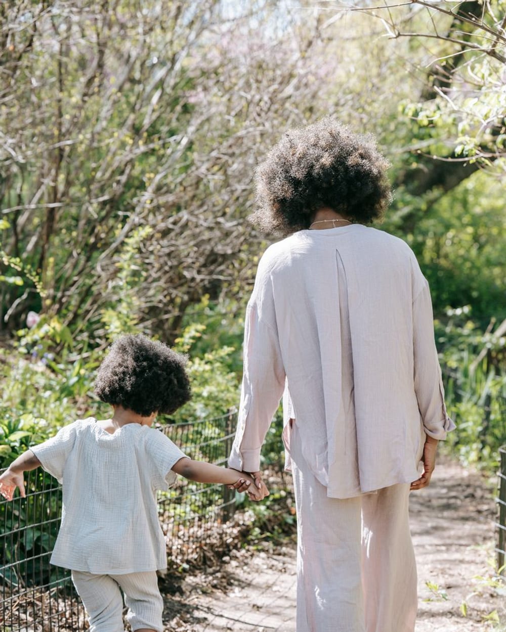 An adult and a child walking together outdoors, holding hands, seen from behind
